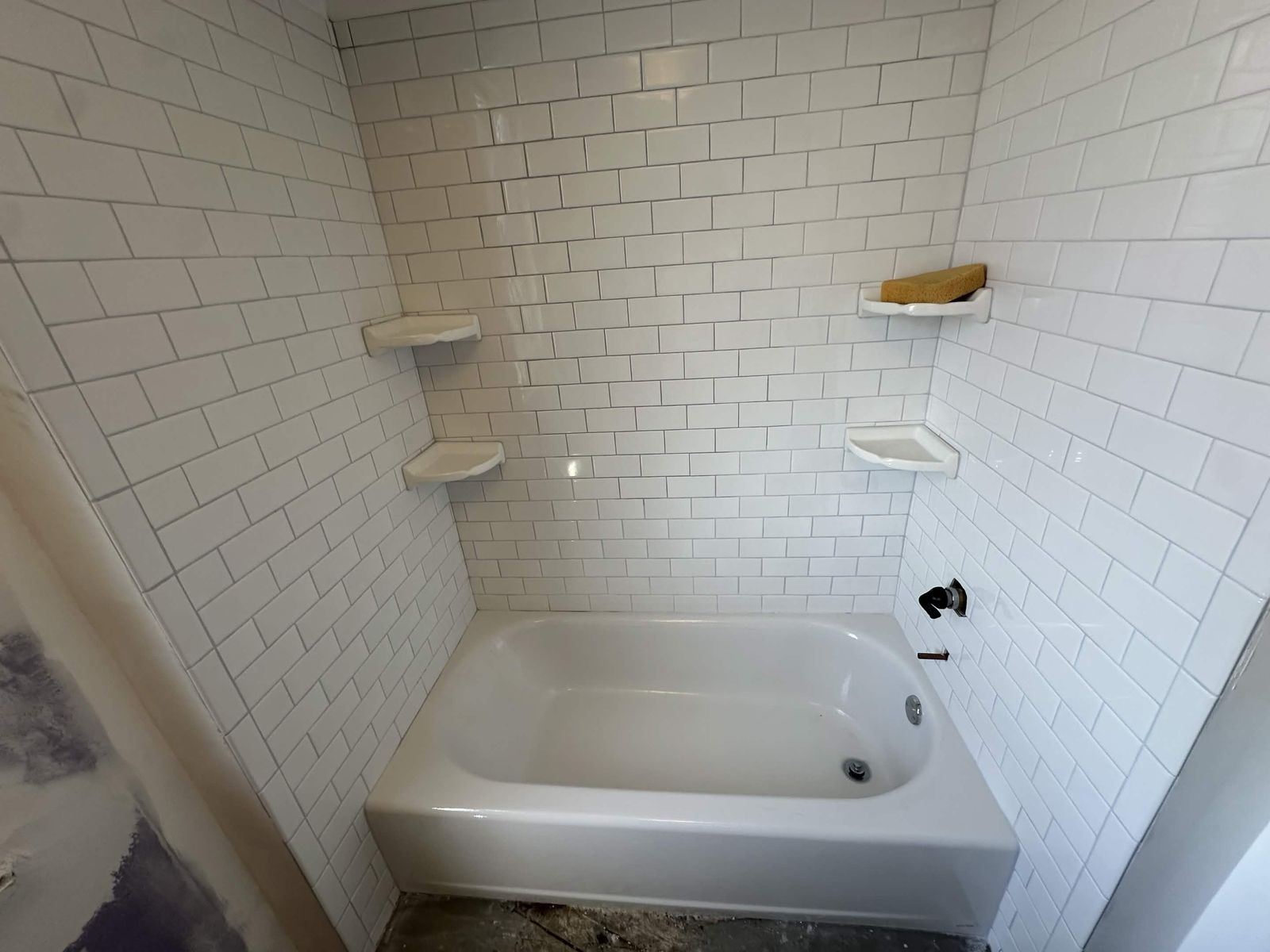 New bathtub with a subway tile surround and corner shelves.
