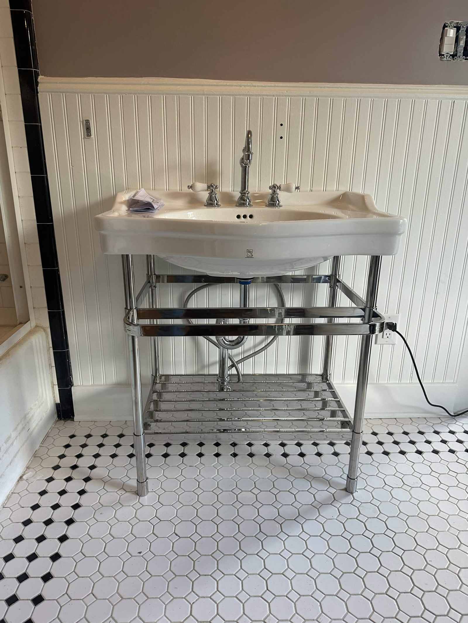 Console sink installed on a new black and white tile floor.