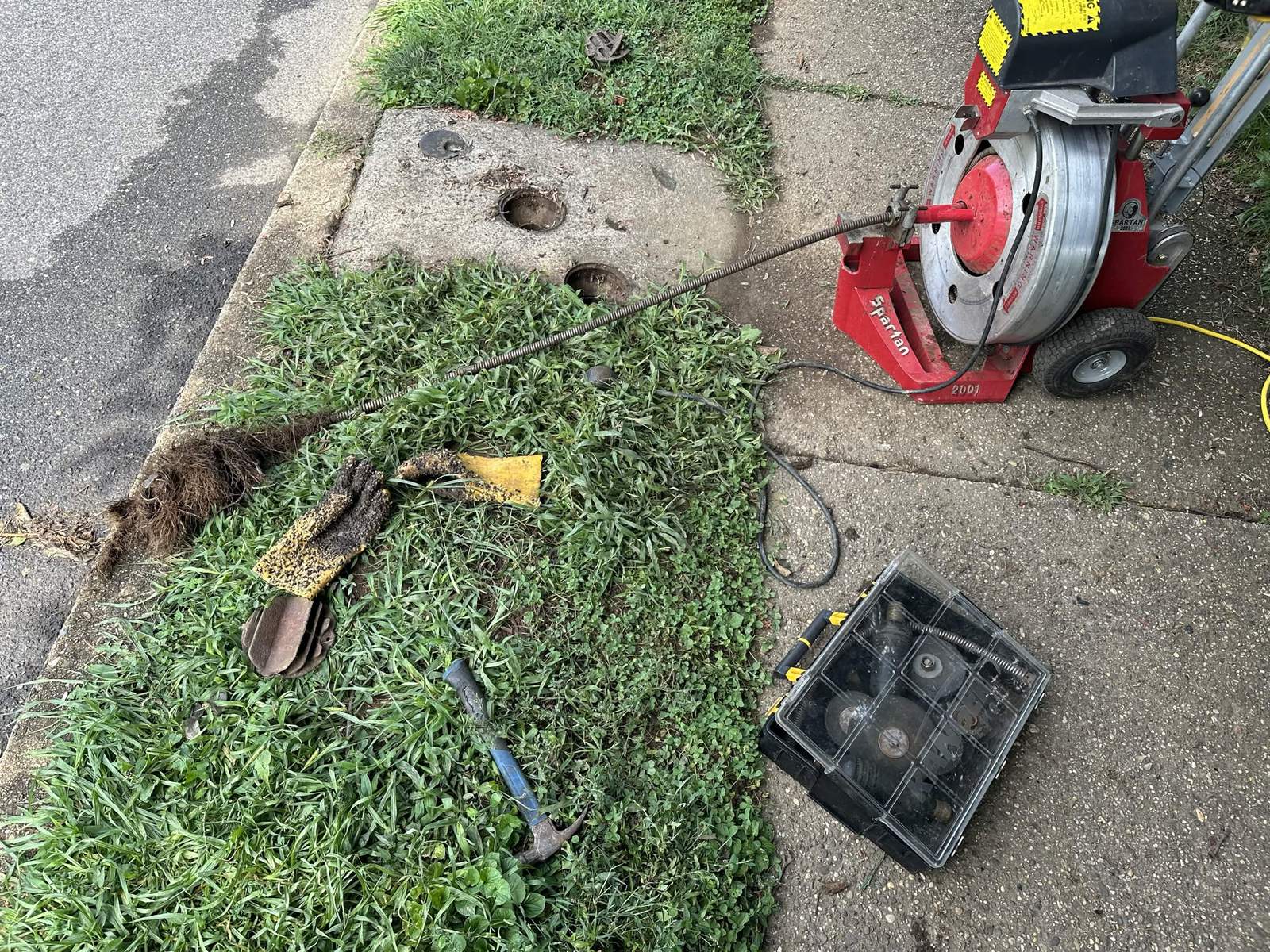Drain cleaning machine at an outdoor sewer access with removed roots beside it.