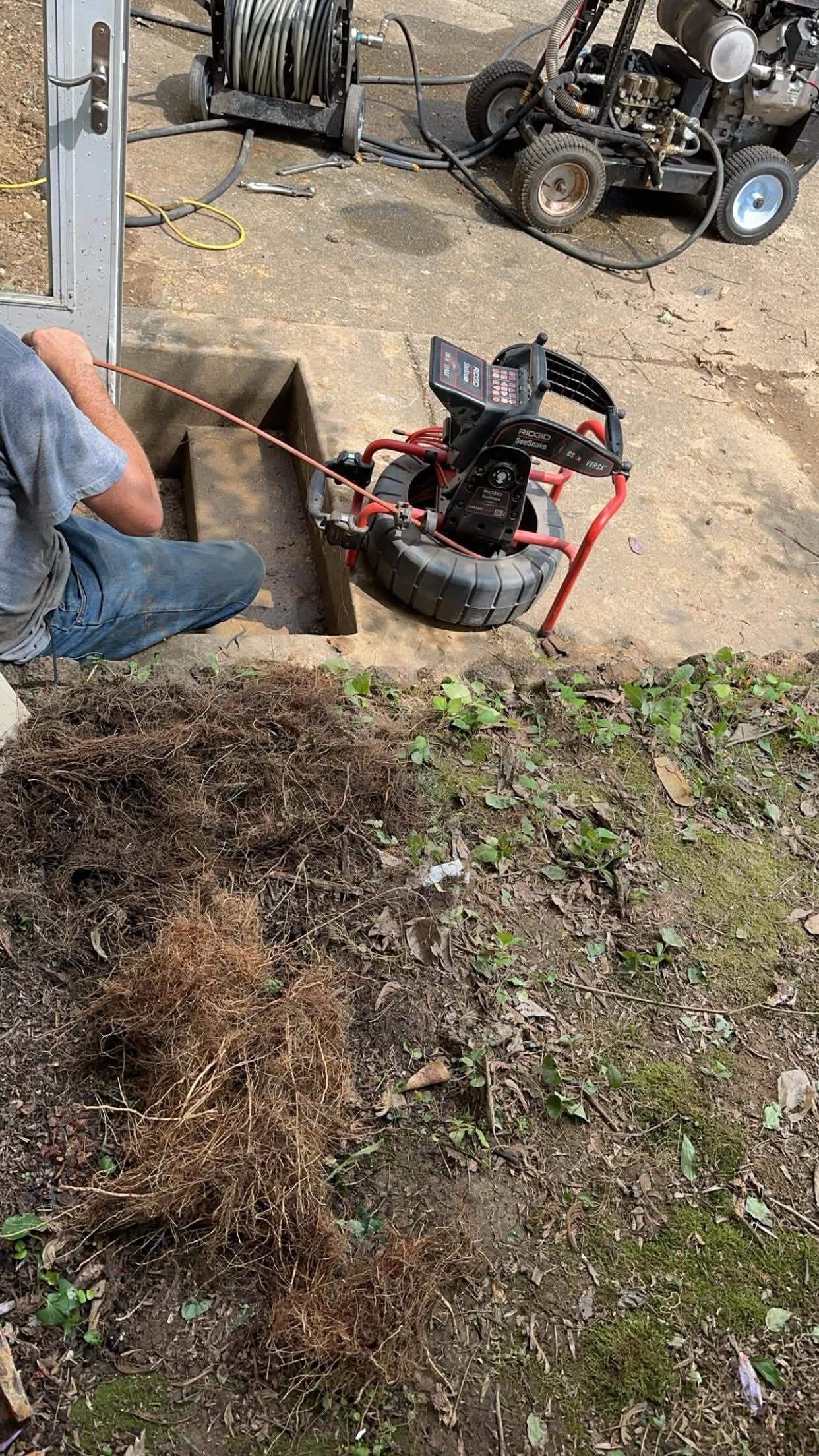 Sewer inspection camera beside an open drain access with removed roots nearby.